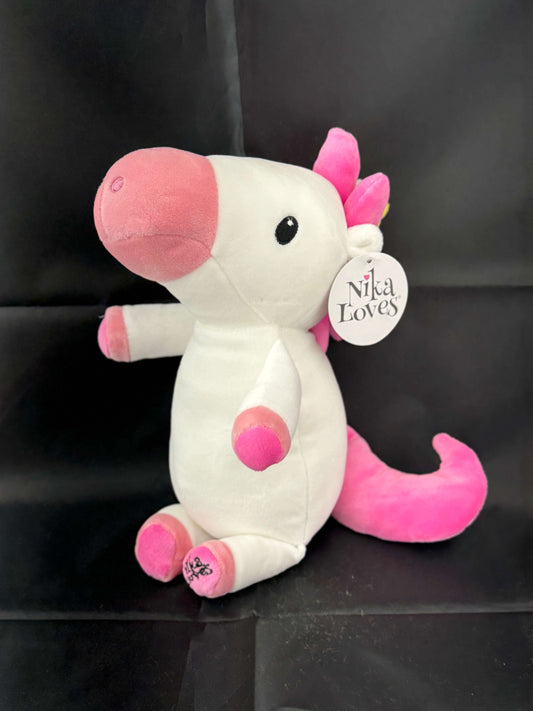 Pink and white plush unicorn toy with a tag labeled "Nika Loves" against a black background.